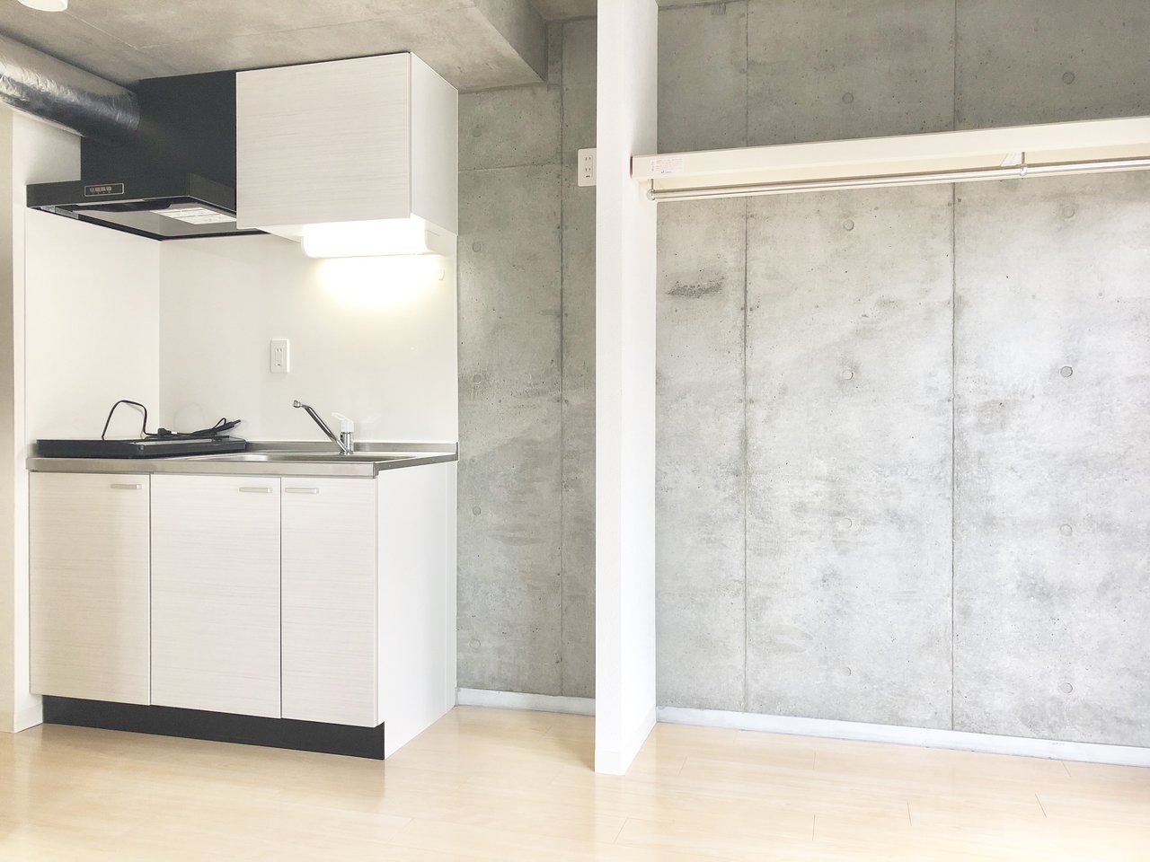 白・黒・グレーのシンプルカラーで統一されたキッチンと居室。キッチンには収納スペースもあり、IHコンロが2口ついていますよ。