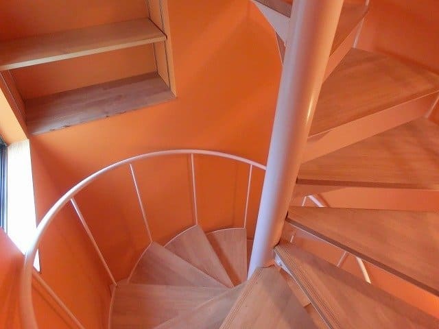 玄関へと続く螺旋階段の周りにはオレンジのクロス。ここにも棚があり、いろんなディスプレイを楽しめます。