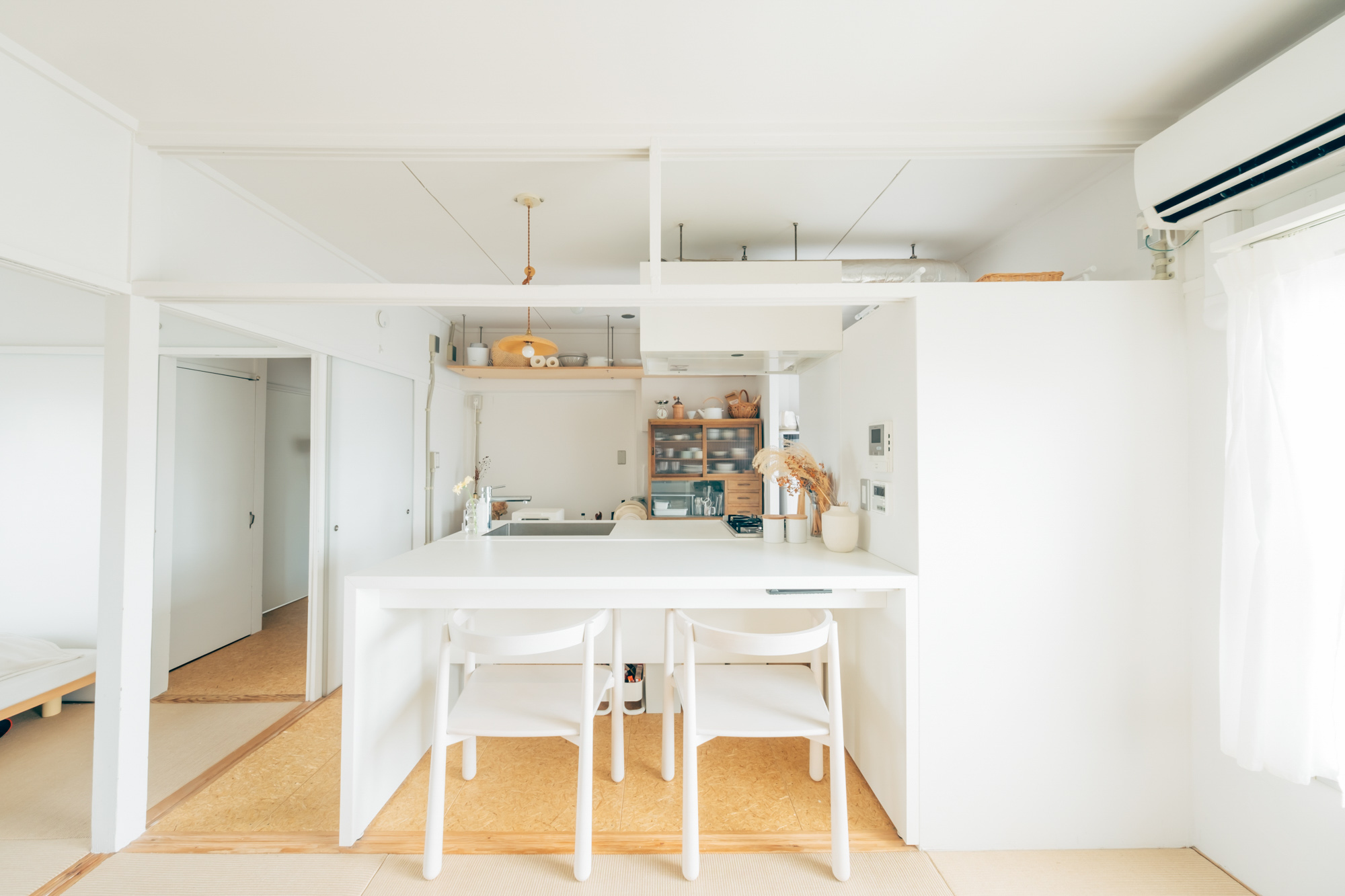 リノベーション団地で二人暮らしをされている方のお部屋。キッチンからまっすぐに伸びた、備え付けの真っ白なテーブルの上に、木製のランプシェードが吊るされて、とても印象的です。