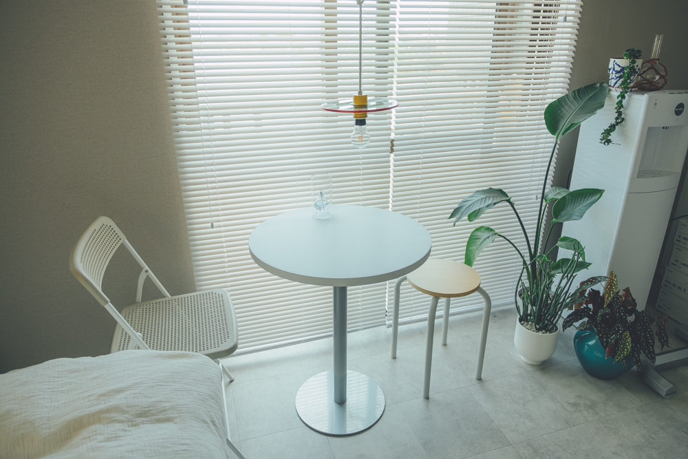 テグスを使って窓際のダイニングテーブルのすぐ上に配置されています。白いブラインド、モルタルの床、白いテーブルと、カラフルなアイテムが映える空間ですね。